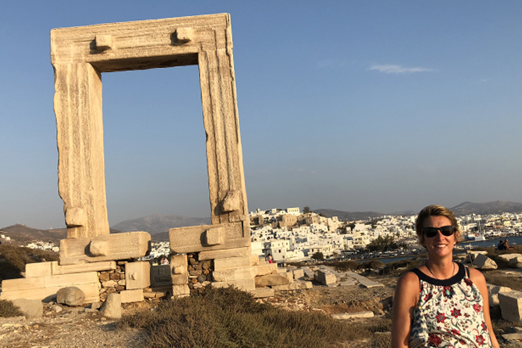 A Woman in Sunglasses and flower pattern top standing in front of a ruined ancient Greek monument