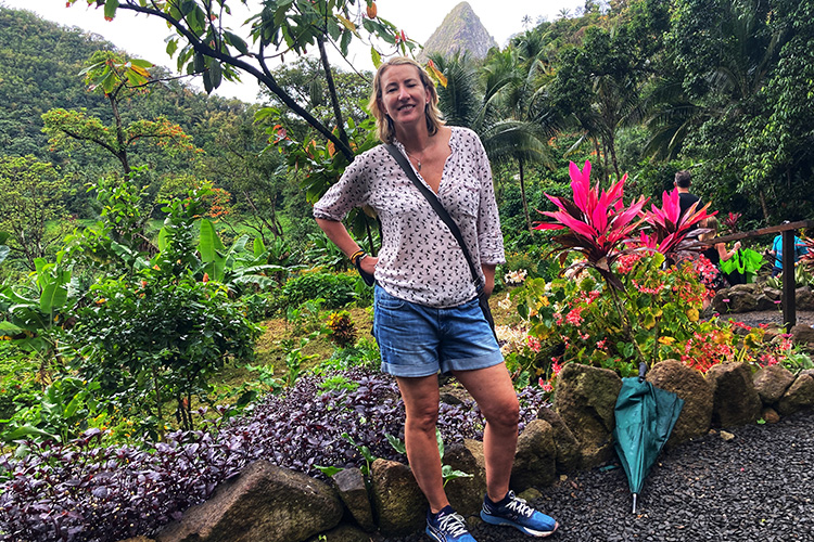 A Woman in a patterned top and denim shorts standing in a tropical garden