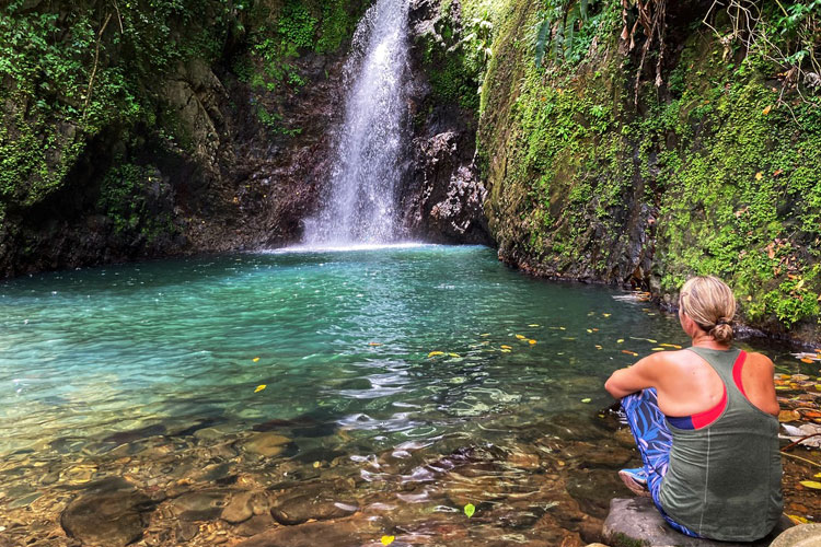 Woman sitting with her back to the camera, watching a waterfall