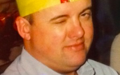 A Man in a yellow Christmas hat winking at the camera