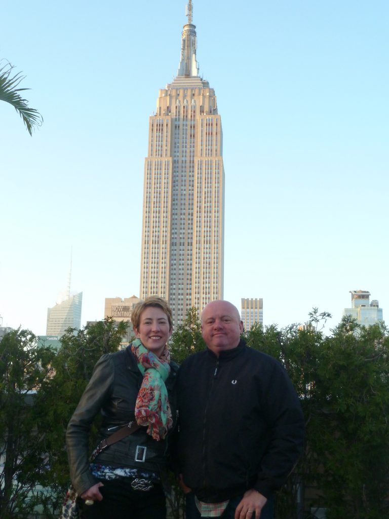 A couple standing by a hedge in new york in front of a tall skyscrapper
