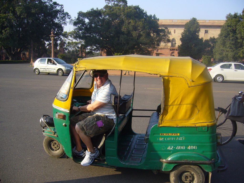 A smiling man driving a small yellow and green tree wheeler