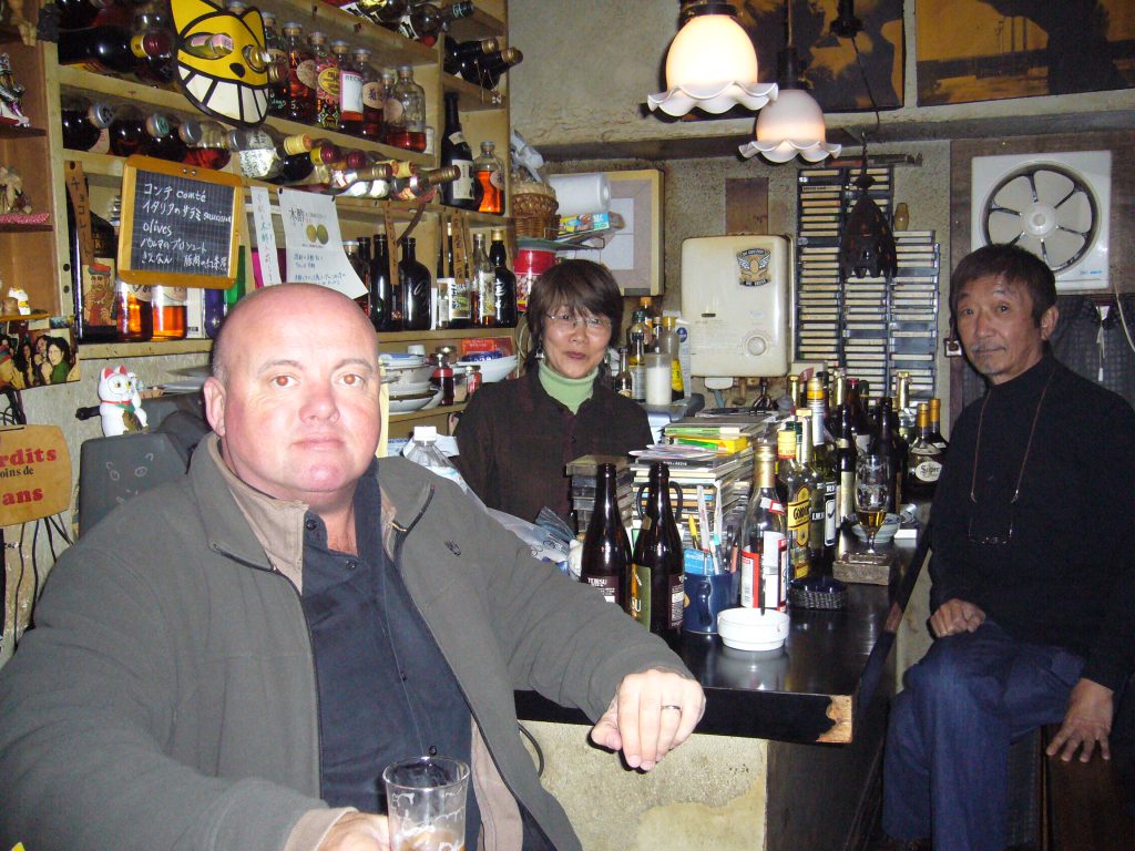 three people sitting in a small well stocked bar 