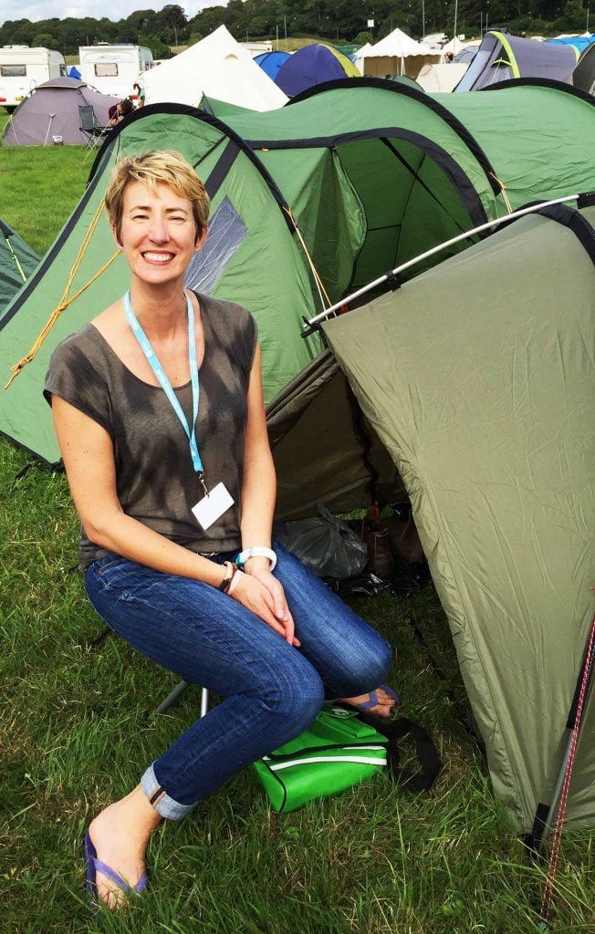 Oxfam volunteer weekend sitting smiling by a small green tent, backstage at Bestival Festival, Dorset England. How To Get A Free Ticket To A UK Music Festival and Help End World Poverty