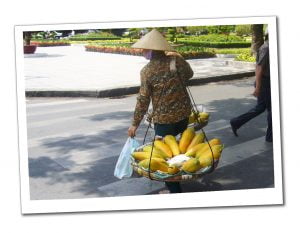 A woman in a traditional hat crosses at a Zebra crossing in Vietnam with a large basket of Yellow Papaya