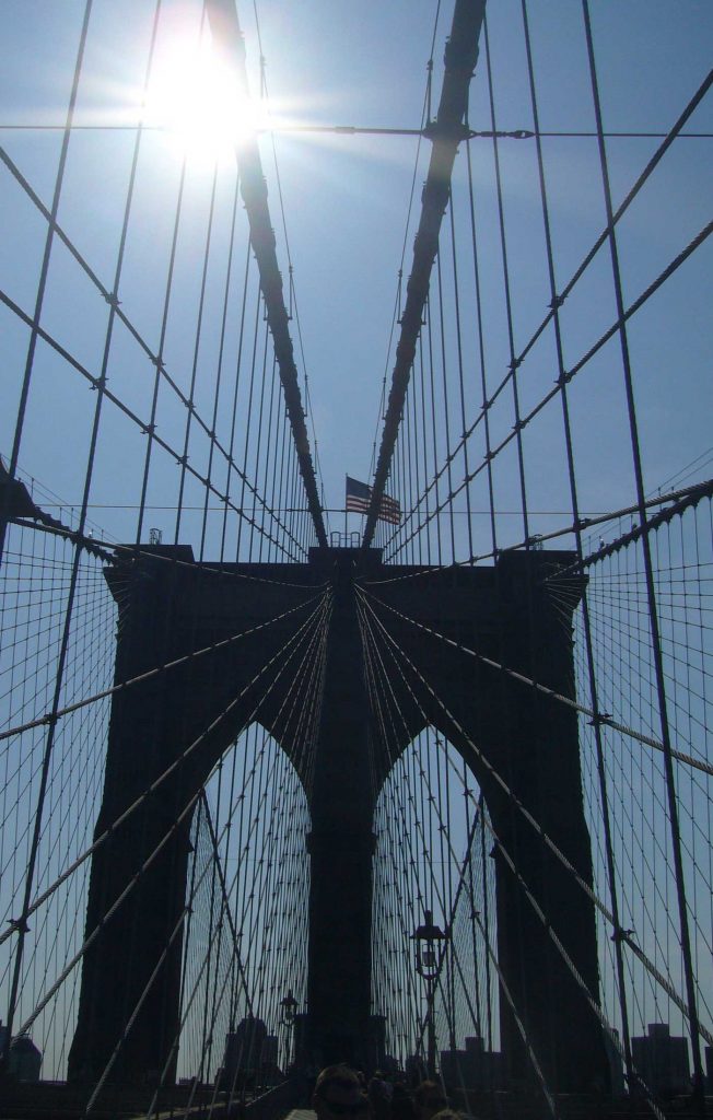 A view looking up at the American flag, The Brooklyn Bridge, New York in the sunshine