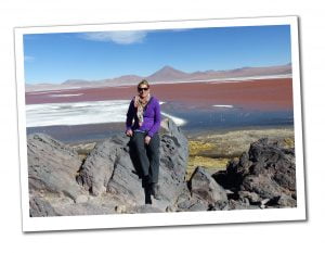 SueWhereWhyWhat sits in front of the pink lake with flamingoes at Laguna Colorada, Bolivia