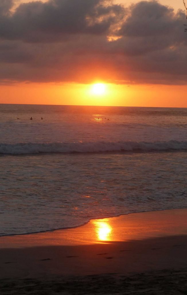 Deep dark burnt umber sky as the sunsets over the still crashing waves at the shore of Santa Teresa beach