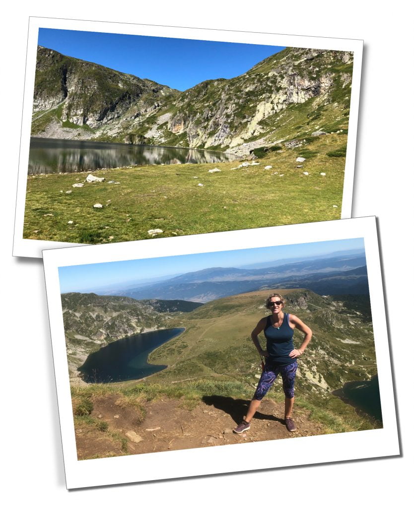 A Woman in dark glasses and sports trousers in front of a kidney shaped lake high on a green hill on a cloudless sunny day
