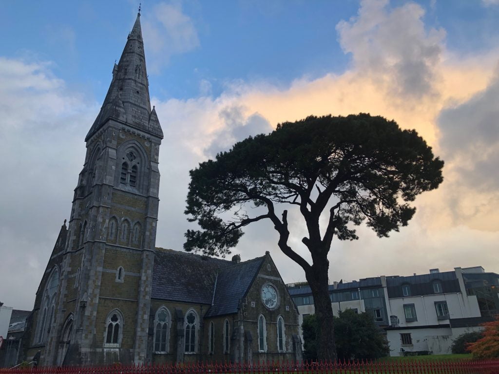 A church and single dark tree in the grey of dusk beneath a pale yellowing sky