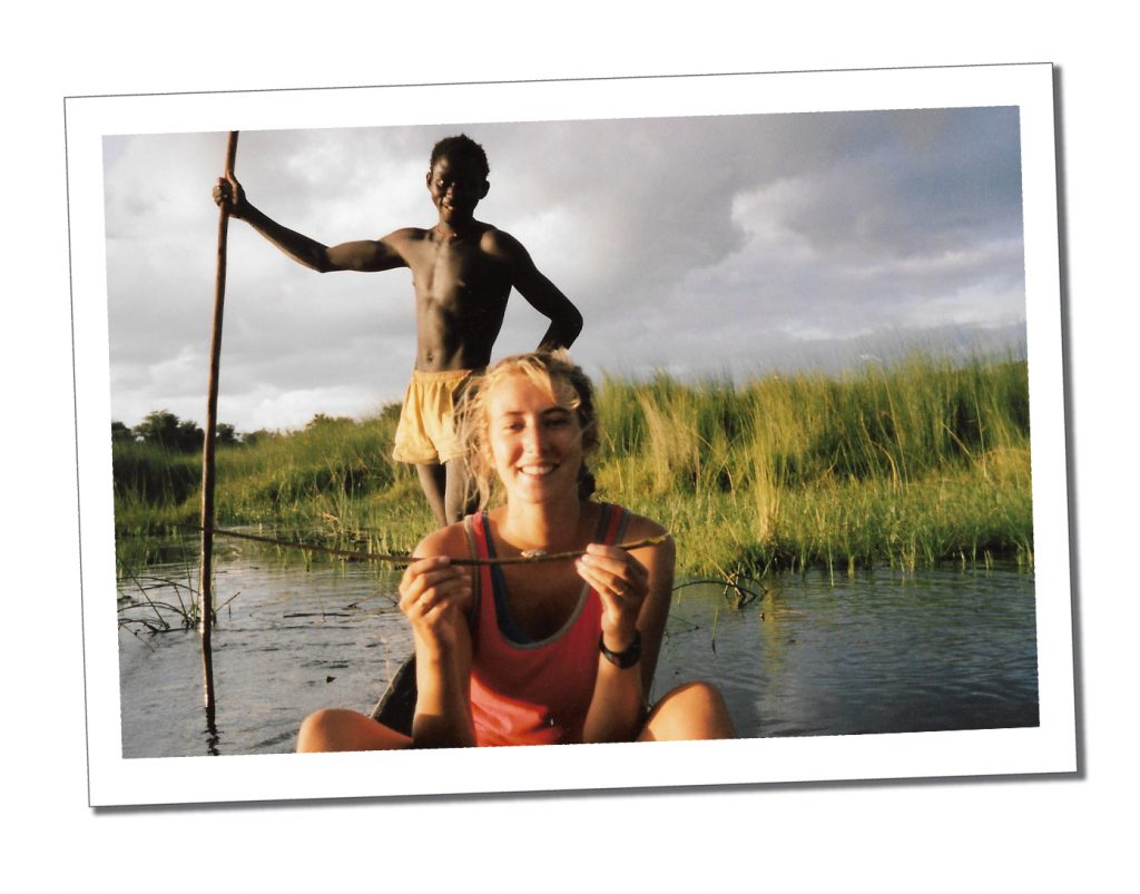 A young woman in an orange top sitting in a boat with a man standing up behind her