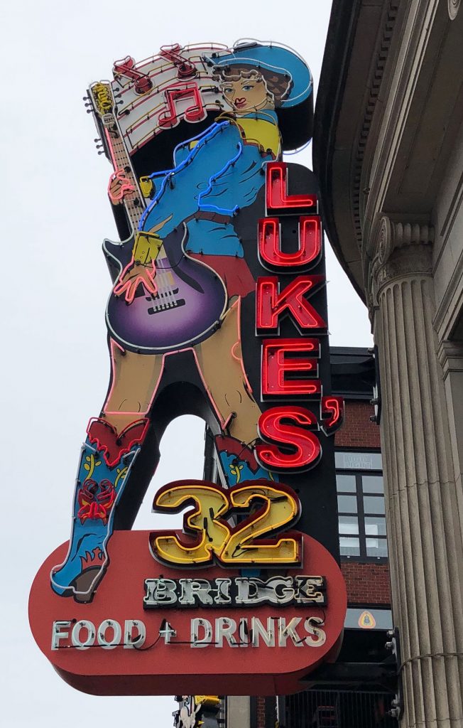 A large neon sign depicting a cowgirl with a purple guitar with the words Lukes 32 running down the length of the sign
