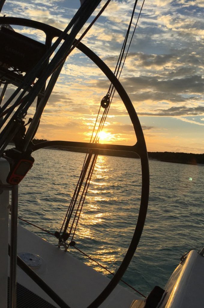 The view through the steering wheel of a yacht to a golden setting sun over a shimmering sea