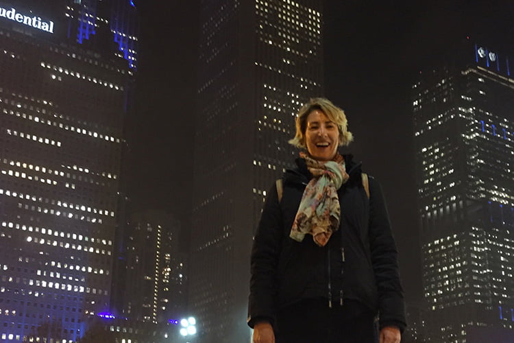 A blonde woman in a black coat smiling in front of the backdrop of dark chicago skyscrapers