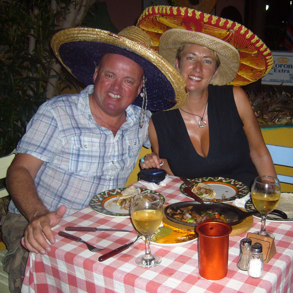 A man and a woman smiling in sombreros at a dinner table with a checked table cloth