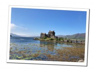 Eileen Donan castle sits serene at the end of a small stone bridge in a blue loch with a purple mountain backdrop