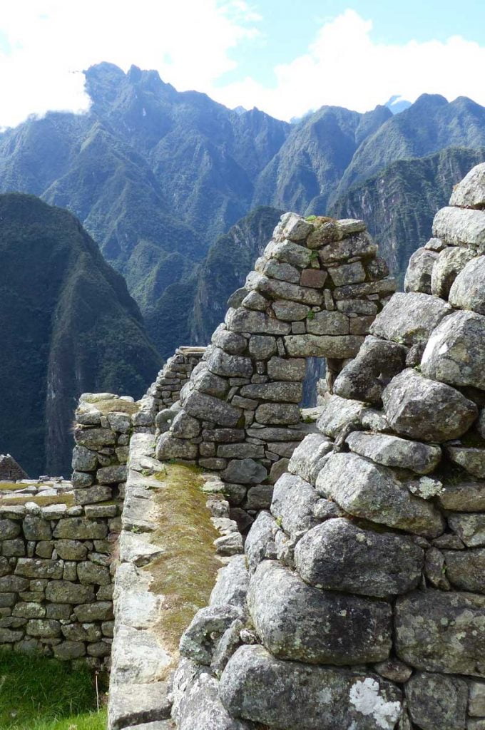 A stunning view from a ruined hut on the mountain side looking down the valley to the river far below, Inca Trail behind her, Peru