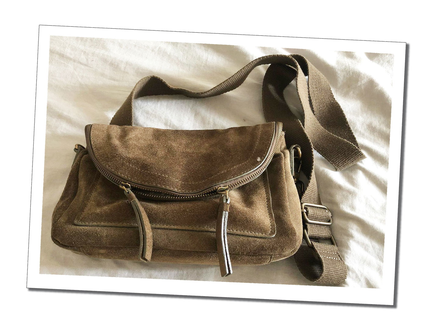 A beige suede shoulder bag laying on a white bed spread