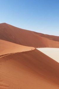 A giant orange sand dune with a tiny person walking across the ridge, Sossusvlei, Namibia