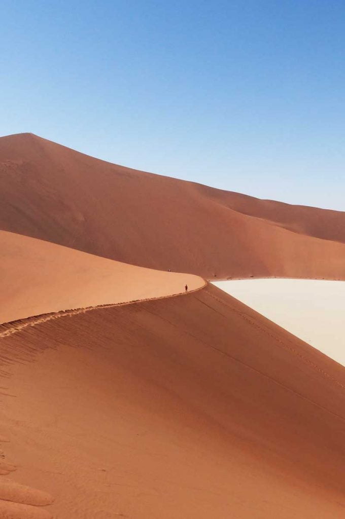 A giant orange sand dune with a tiny person walking across the ridge, Sossusvlei, Namibia