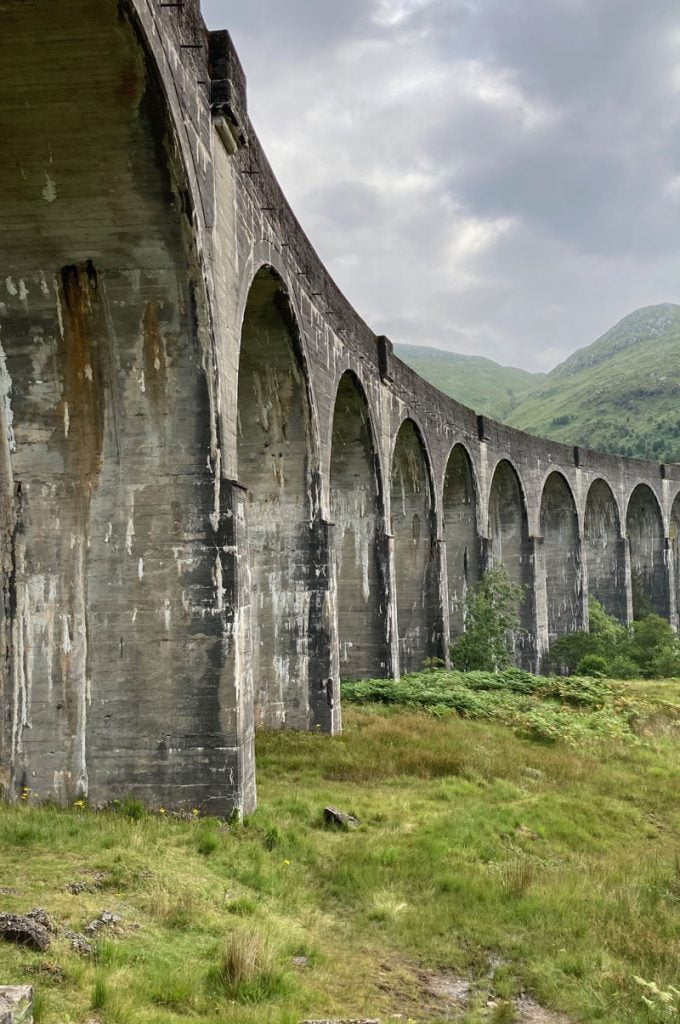 A large stone viaduct arcs in a semi circle in picturesque mountain scenary