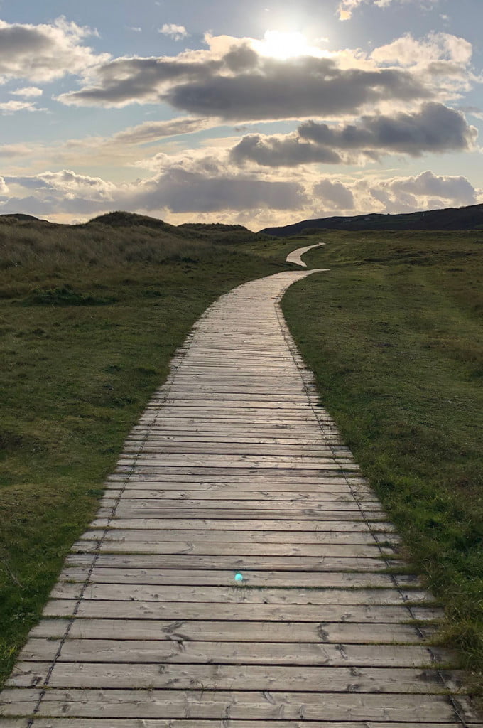 A wooden walkway stretches off into the distance as the sun breaks biblically from behind the clouds