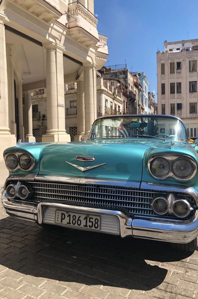 A blue vintage car parked in front of a white pillared building