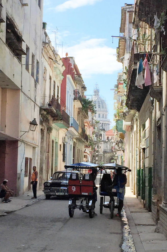 Views of the thin vibrant streets of Havana in Cuba, with people, vintage cars and two seater 'tuc tuc' style 3 wheeled bikes going about their day