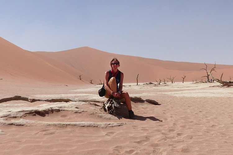 A woman in sunglasses sitting on a low rock alone in a desert landscape