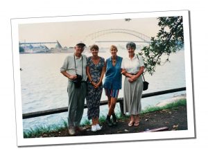 A family group stand by the waters edge with a view of Sydney Harbour bridge beyond