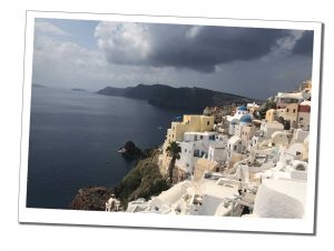 Slate grey skies with a hint of sunlight over the beautiful panorama of Santorini's whitewashed buildings that cling to the hillside overlooking the bay.