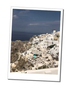 The white washed buildings of Oia, Santorini, clinging to the cliffs under a dark and brooding sky, Greek Islands