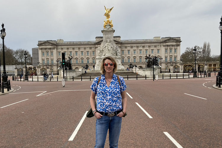 A Woman in a blue flowery shirt standing in the mall in front of Buckingham Palace