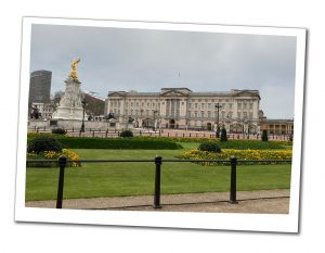 The front of Buckingham Palace and manicured gardens in front with overflowing borders of yellow flowers