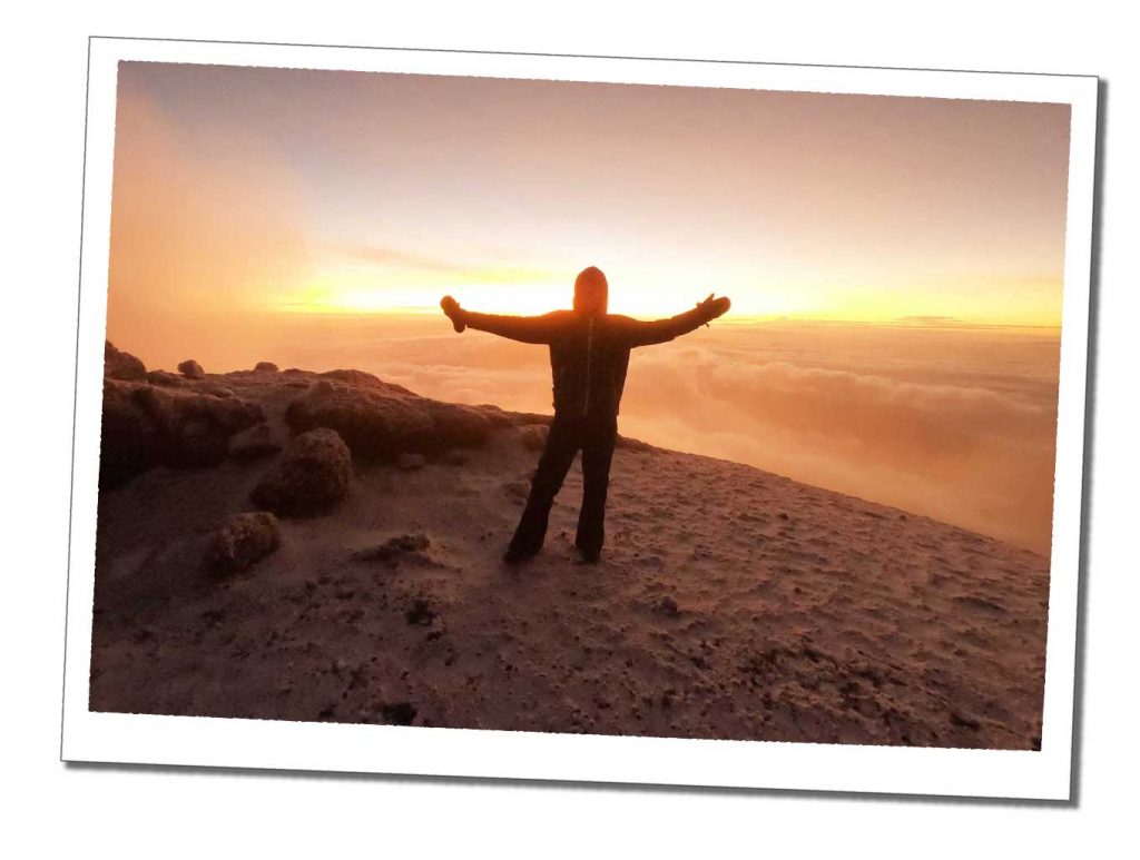 A Woman standing in silhouette at sunrise at the top of a frozen snowy mountain
