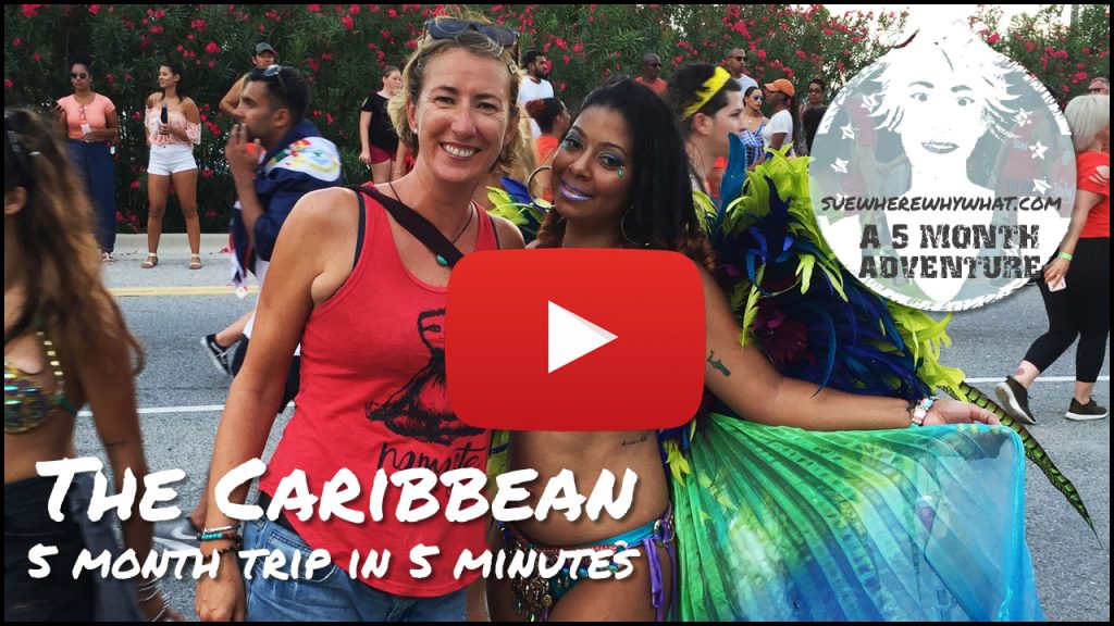 A blonde woman & bikini clad revellers in feathered headresses & beachwear parade up the street, Cayman Carnival Batabano. 5 Month Self Tour of The Caribbean