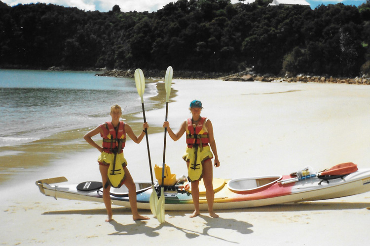 Two women standing on a beach with canoes and holding paddles