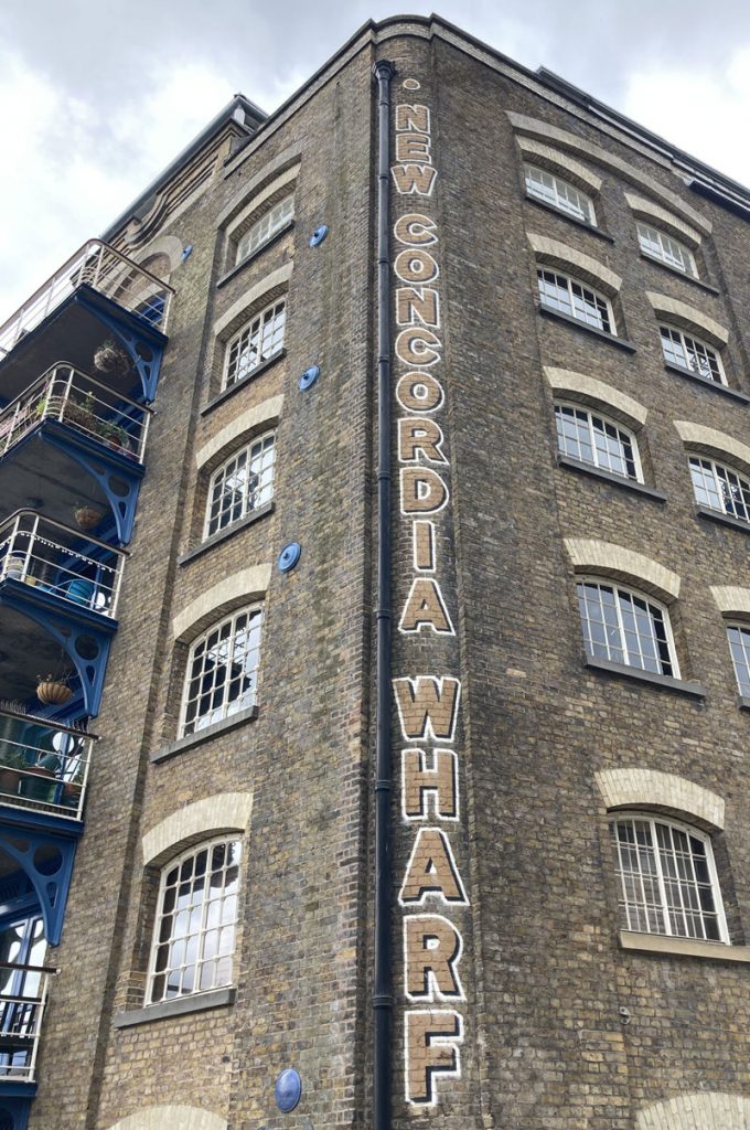 The side view of an old brick warehouse in londons canary wharf with the words New Concordia Wharf printed down it