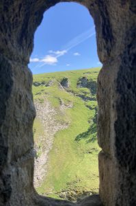 The view from a stone castle window out onto a bright green rocky hill