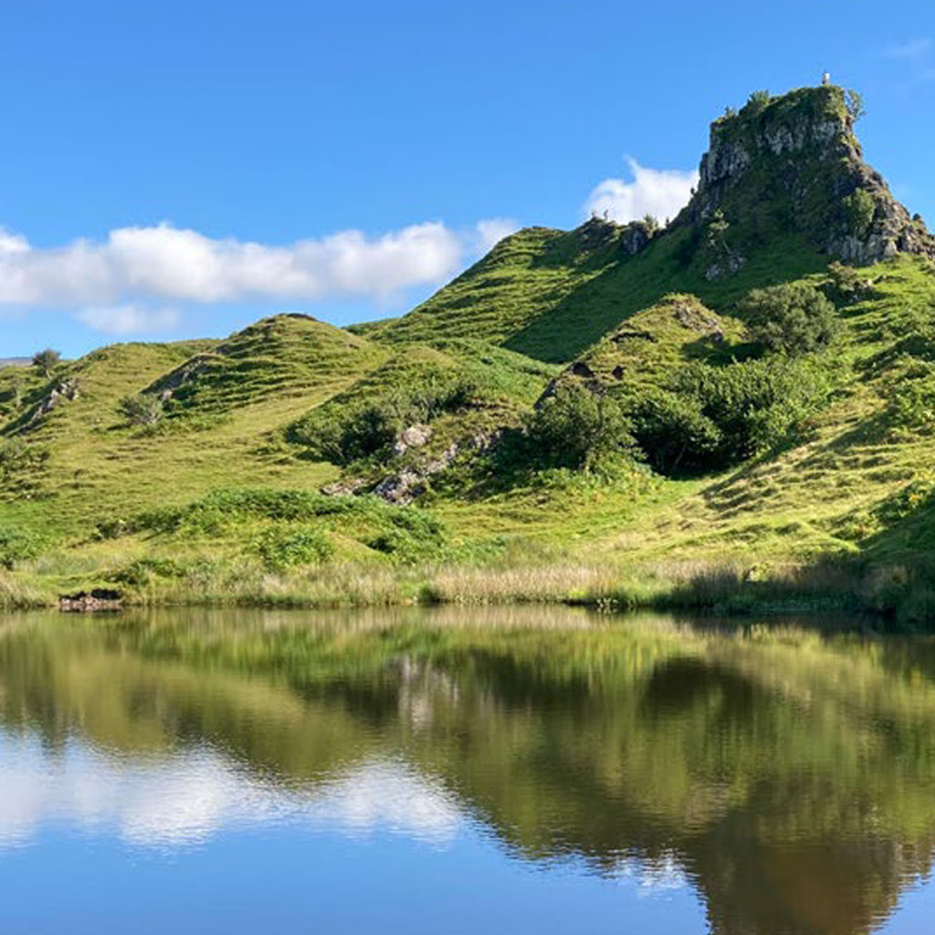 A calm reflective lake with craggy hills at it's shore