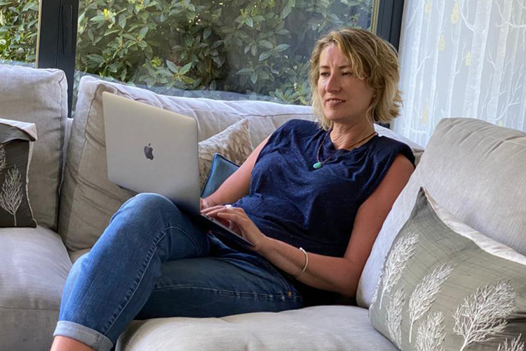 A blonde woman sitting on a sofa looking at an apple laptop