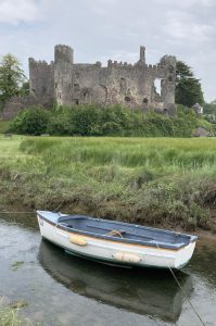 A rowing boat sitting in a low river with the backdrop of a ruined castle behind
