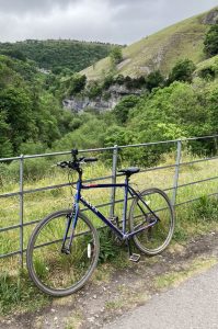 A lone blue bicycle leaning against a metal fence on a bridge over looking a lush green valley in the English countryside
