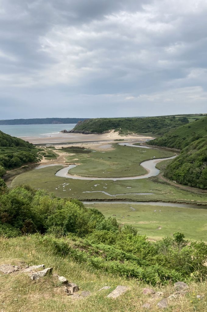 A river snakes it's way across the plain seen from a green fern covered hill overlooking a sandy bay