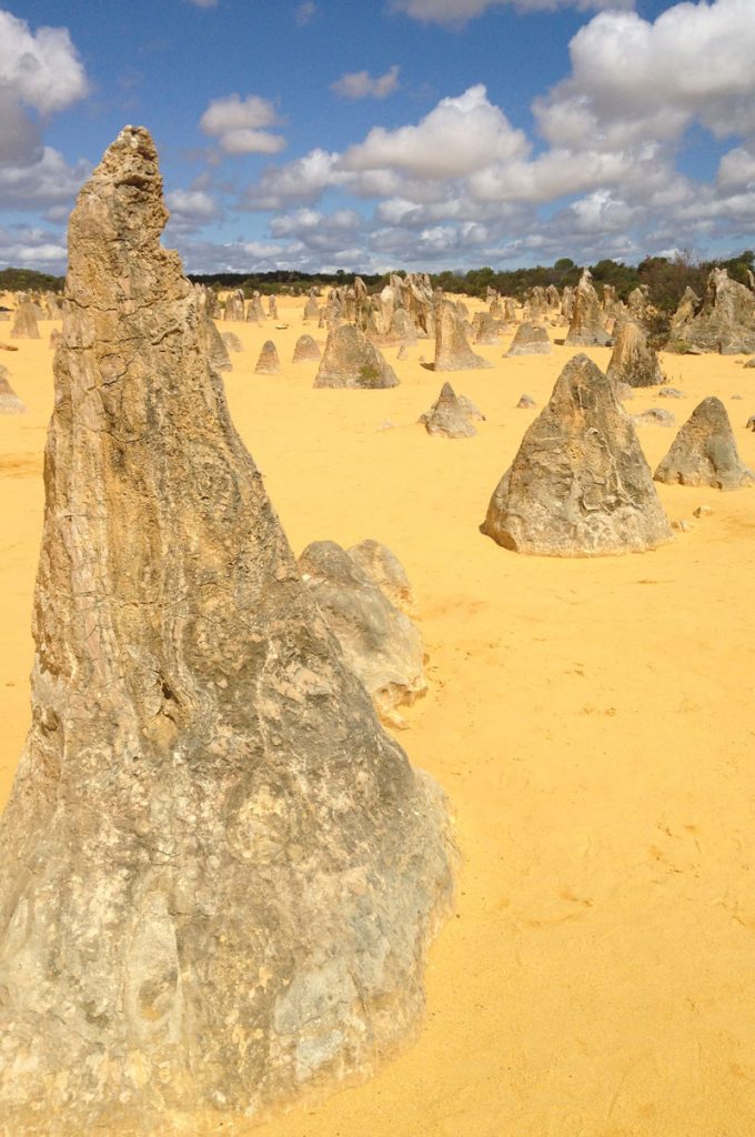 Large cone shaped 'Pinnacle' stones on bright orange sand under a cloudy bright sky