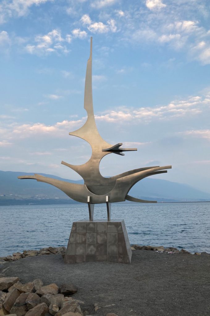 A large metal viking ship sculpture standing by a large lake