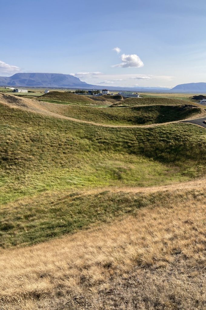 Remote grass covered hills with circular craters and thin man made paths next to a lake