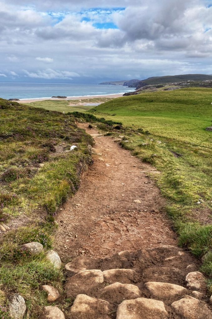 A rough rocky path in green moorland leading to the sea on
