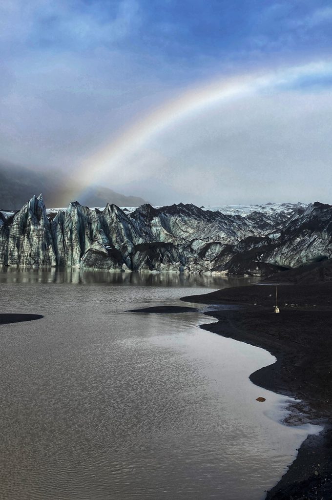 A rainbow high above a still glacial landscape