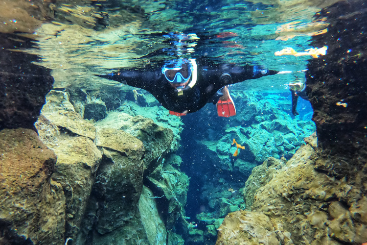 A Woman in a snorkel swimming towards the camera in blue water between two large rocks